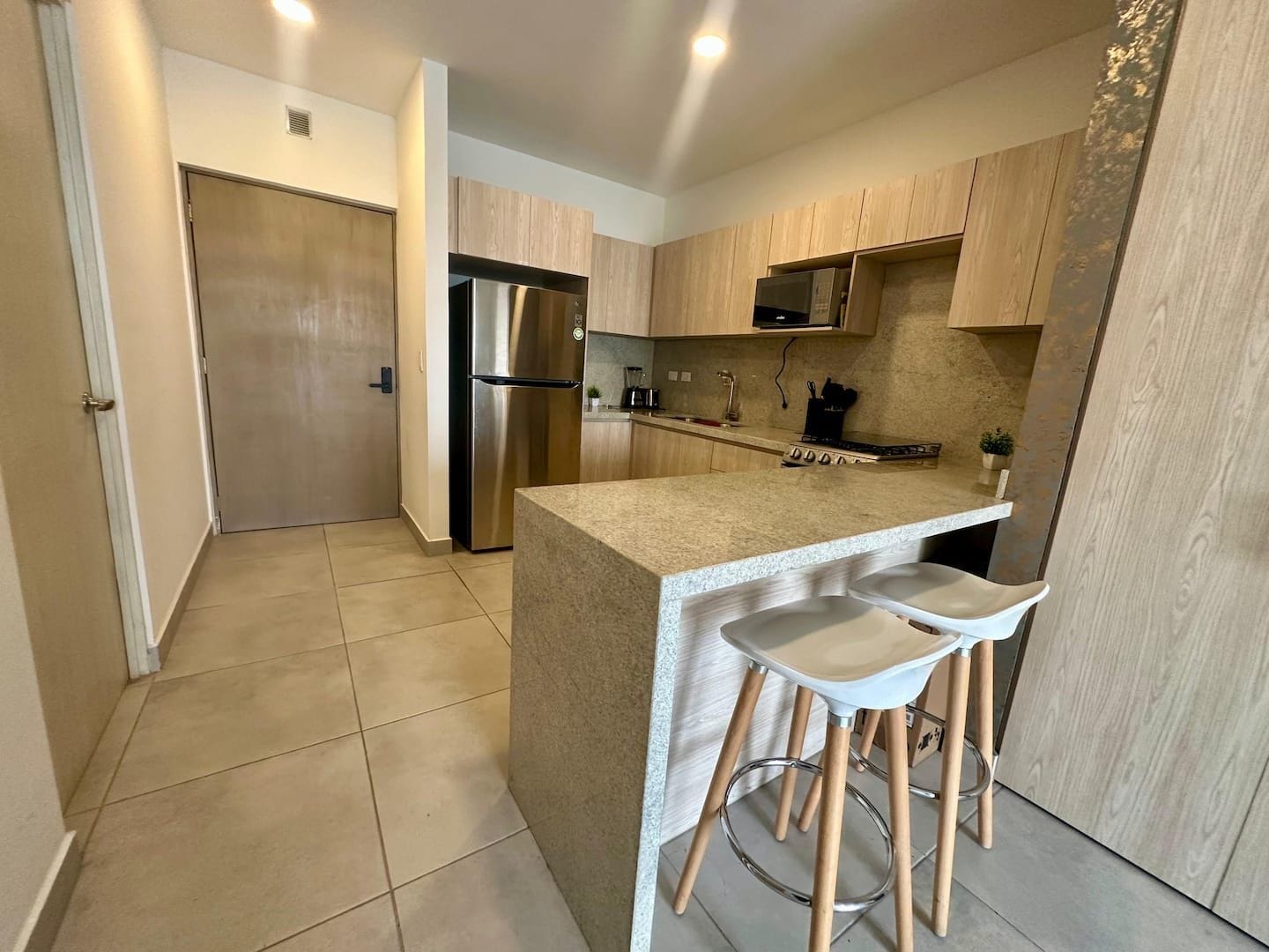 A modern kitchen with a stainless steel refrigerator, wooden cabinets, and a central island with bar stools.