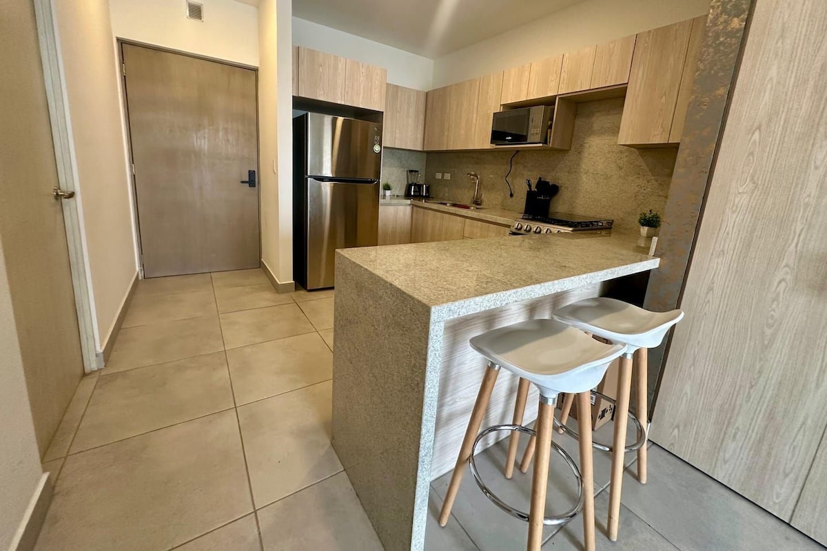 Uma cozinha moderna com geladeira de aço inoxidável, armários de madeira e uma ilha central com banquetas.