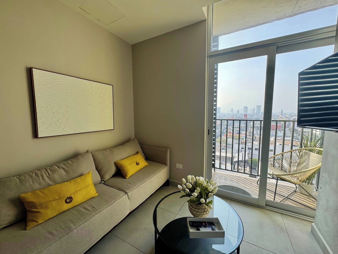 Un moderno salón con sofá, una mesa de centro y vistas a la ciudad a través de un gran ventanal.