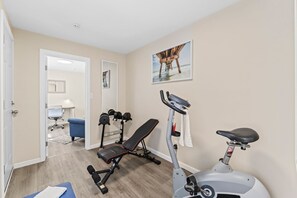Ein Heimfitnessraum mit Trainingsgeräten, darunter eine Hantelbank, Kurzhanteln und ein Crosstrainer.