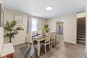 Un coin repas avec une table et des chaises en bois, un réfrigérateur et un escalier.