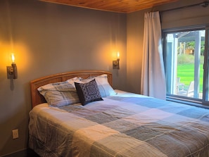 Ein Schlafzimmer mit einem Bett, zwei Wandleuchten, einem Fenster mit Vorhängen und Blick ins Freie.