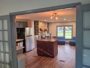 A modern kitchen with a stone wall, wooden cabinets, and a built-in island. - Caberfae Cabin - 3BR Next to Caberfae Peaks Ski & Golf Resort (Cadillac)