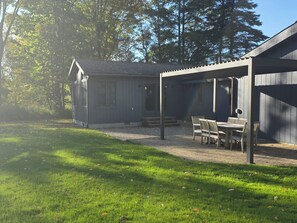 A covered outdoor seating area with a table and chairs, adjacent to a building with a sloped roof. - Caberfae Cabin - 3BR Next to Caberfae Peaks Ski & Golf Resort (Cadillac)