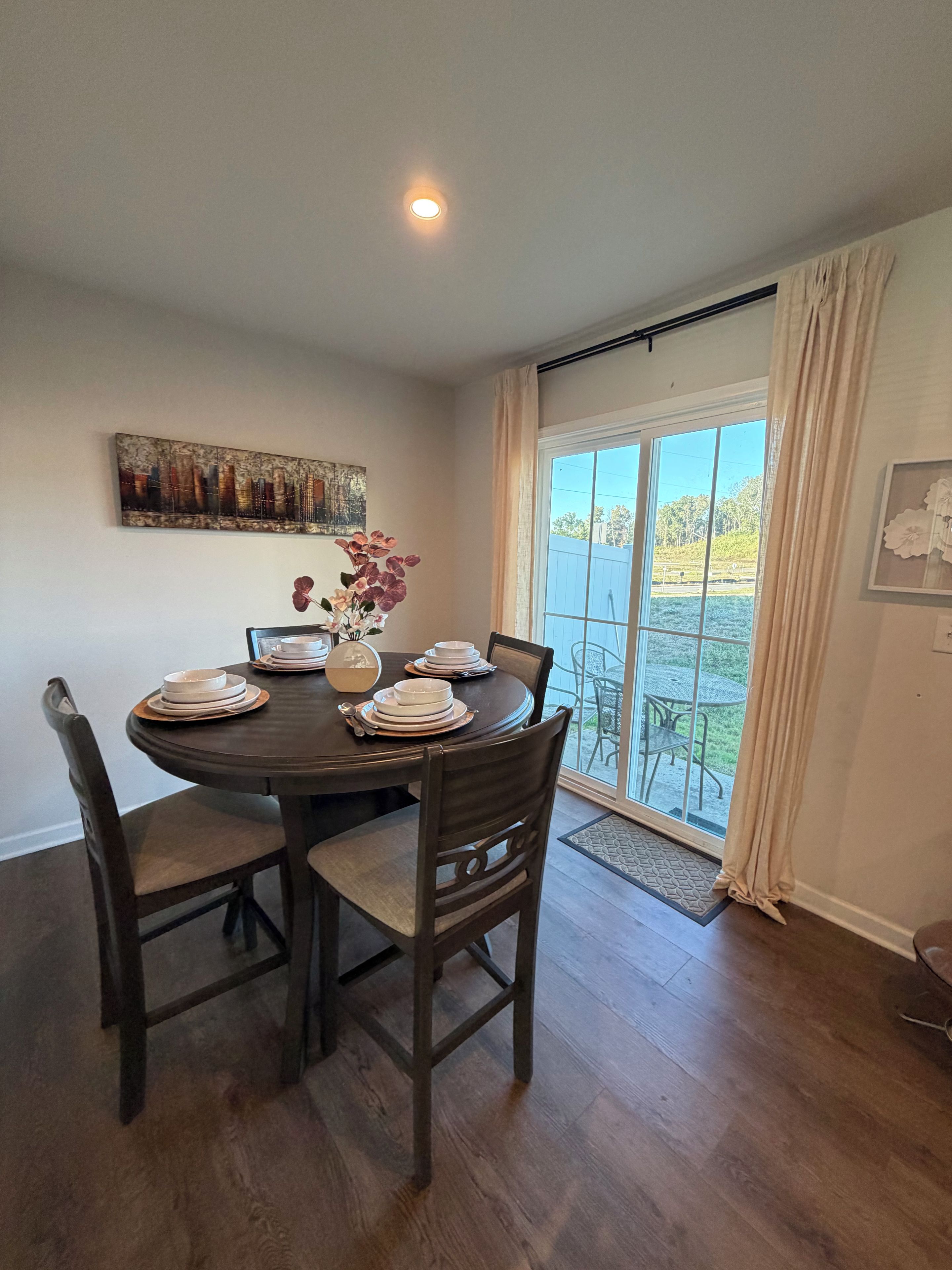 A dining area with a round table set for four, surrounded by wooden chairs.