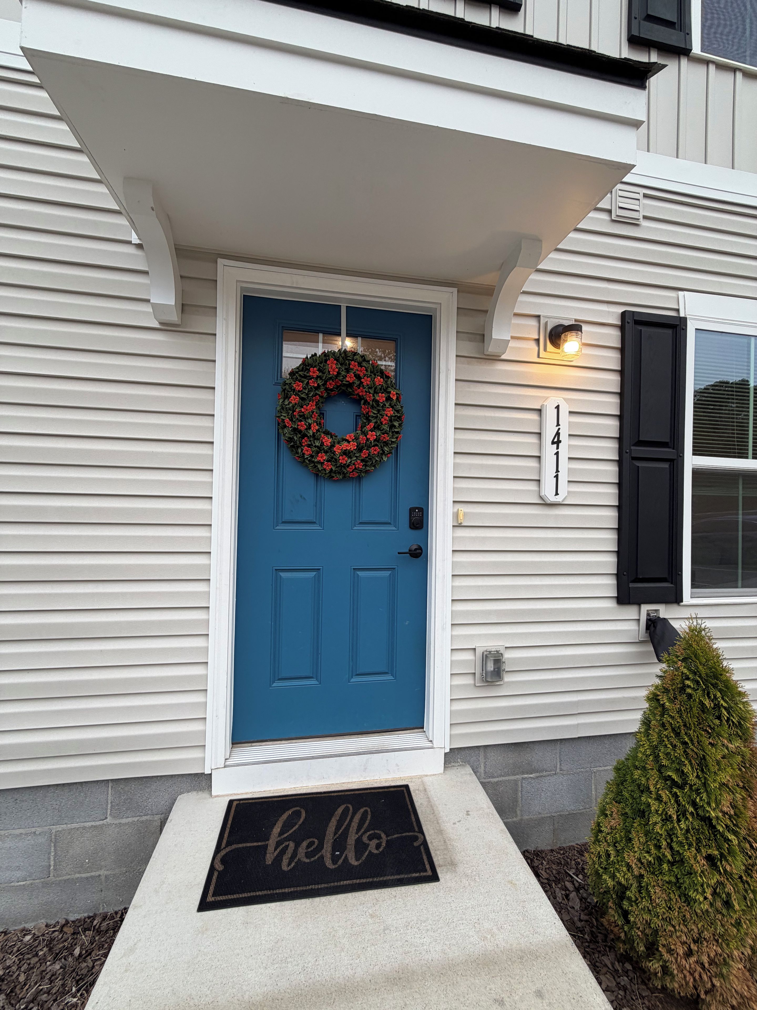 Une maison avec une porte bleue, une couronne décorative, un paillasson sur lequel est écrit « Bonjour » et une boîte aux lettres.