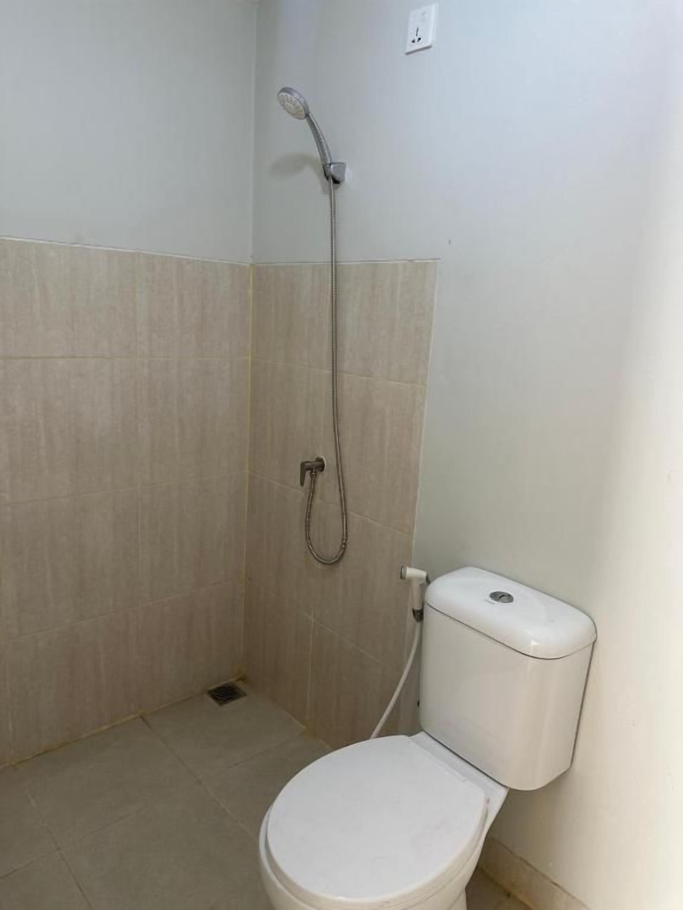 A bathroom with a toilet, a shower, and a wall-mounted toilet paper dispenser.