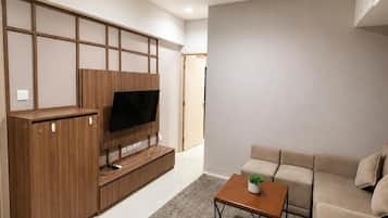 Een moderne woonkamer met een flatscreen televisie, een houten entertainmentmeubel, een beige bank en een klein bijzettafeltje met een plant.