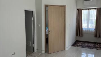 Una habitación amplia con suelo de baldosas, puerta de madera, ventana con cortinas y un ventilador de techo.