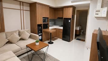 Een moderne woonkamer met een bank, salontafel en televisie. Grenzend is een compacte keuken met een koelkast, magnetron en spoelbak.