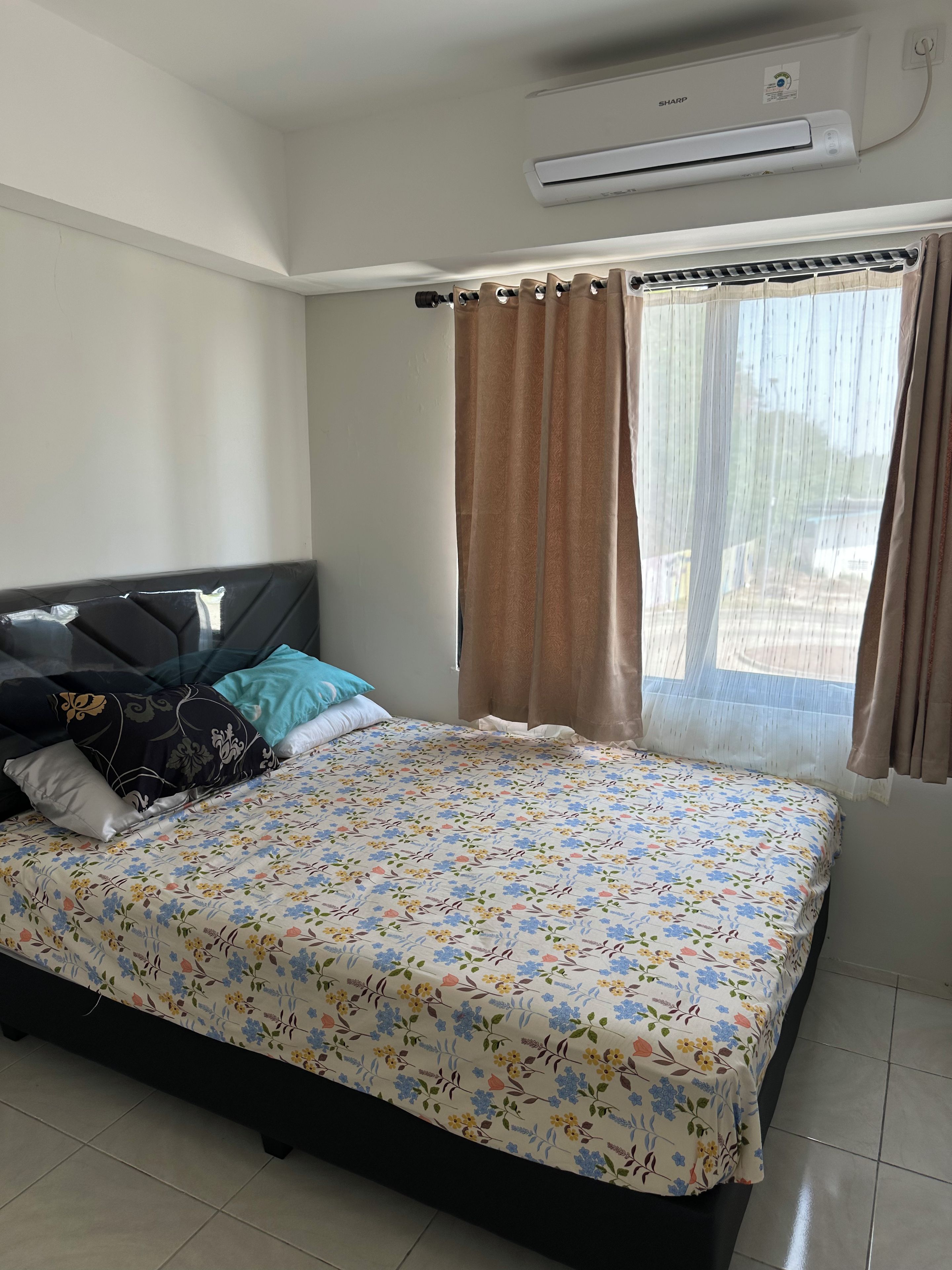 A bedroom with a bed, pillows, a window with curtains, and an air conditioning unit.