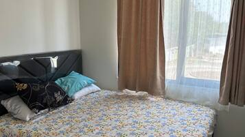 A bedroom with a bed, pillows, a window with curtains, and an air conditioning unit.