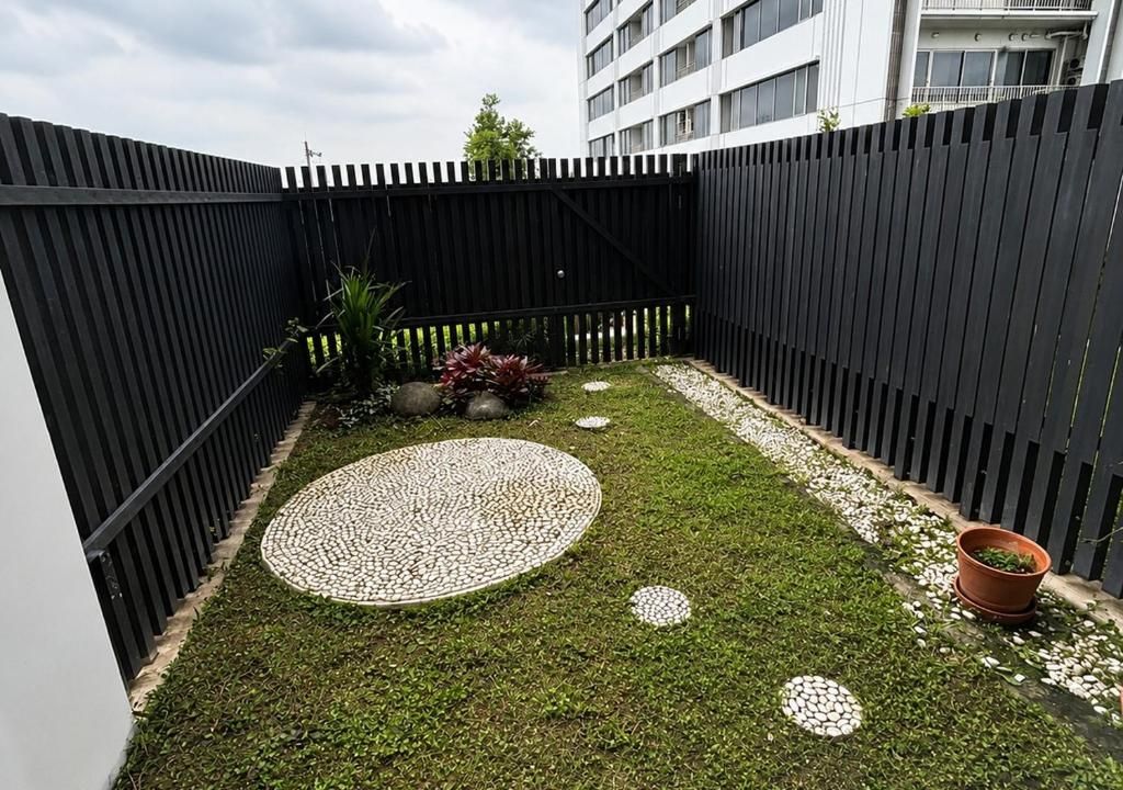 A fenced outdoor area with a circular patterned stone path, a small garden with potted plants, and a building in the background.