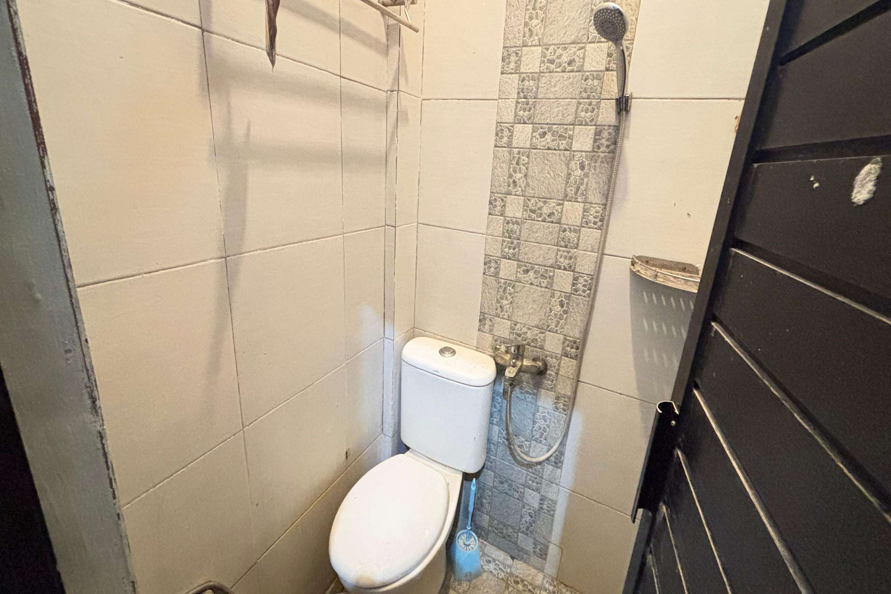 Un baño pequeño con azulejos, un inodoro, una ducha y una puerta negra.