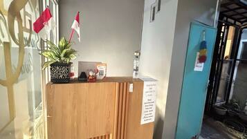 Balcão de madeira na recepção, com planta em vaso, bandeira e placa com informações sobre check-in e check-out.