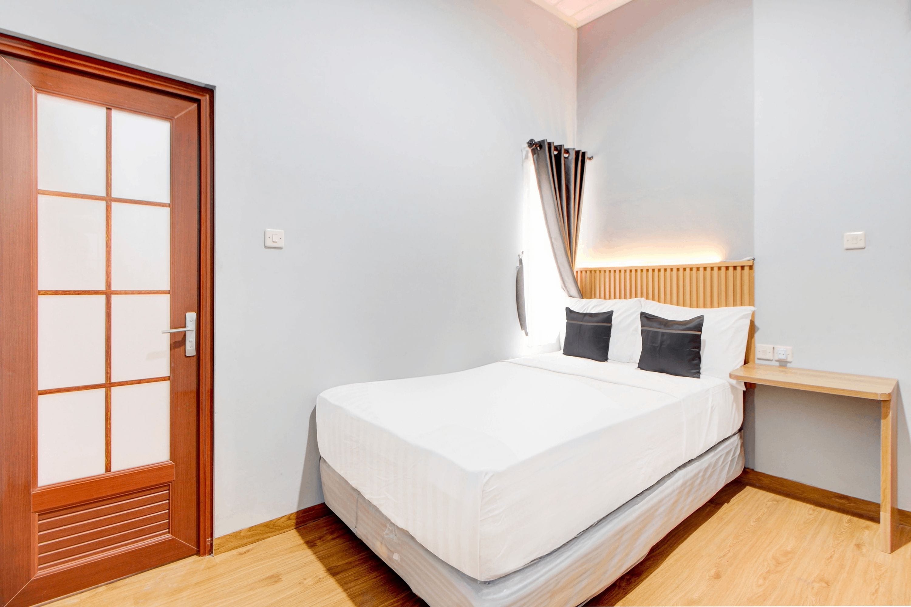 Un dormitorio con puerta de madera, una cama con ropa blanca, una mesita de noche y una lámpara de noche.