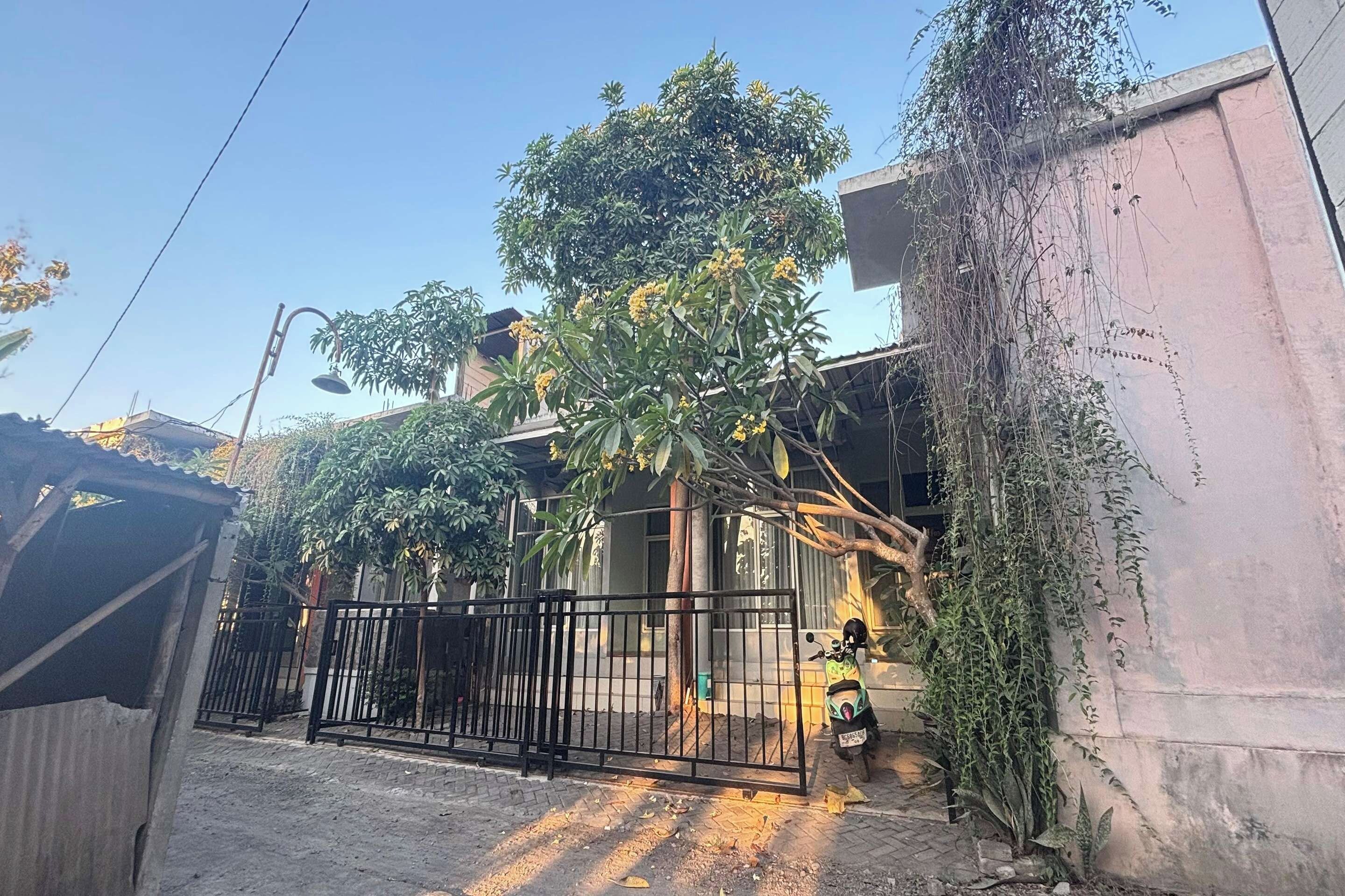 Zona residencial com portão fechado, árvore florida em amarelo e uma scooter estacionada.