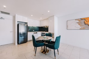 Una cocina moderna con armarios blancos, un refrigerador negro y sillas color turquesa alrededor de una mesa redonda.