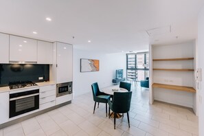 A modern kitchen with white cabinets, a gas stove, and a dining area with a round table and chairs. - Refined One Bedroom Retreat (Fortitude Valley)