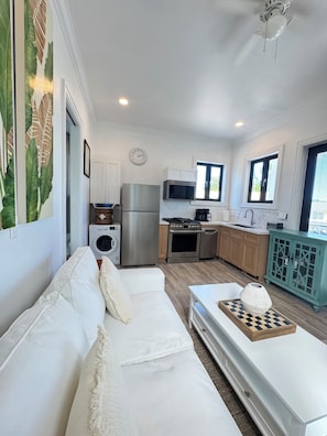 A modern kitchen with stainless steel appliances, a dining area with a white table and a chessboard, and a living area with a white sofa. - Cozy studio in walking distance to restaurants, marinas, coffee shop & groceries (Marsh Harbour)