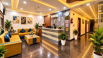 A hotel lobby with a reception desk, seating area, and a staircase.