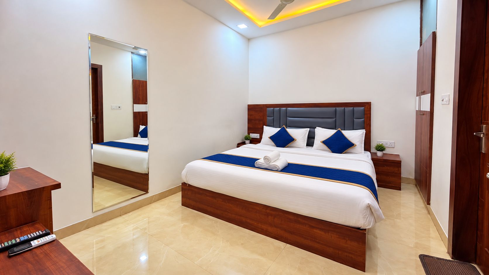 Une chambre d’hôtel moderne avec un grand lit, une tête de lit en bois, une table de chevet avec une lampe et un miroir au mur.