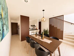 Un espace de salle à manger moderne avec une longue table, des chaises noires et un luminaire suspendu.