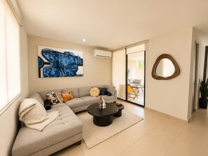 A modern living room with a sectional sofa, a coffee table, and a large abstract painting on the wall. - Cumbres Novonorte: Private Pool, Covered Terrace & 3 Bedrooms (Mérida)
