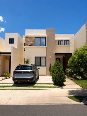 A modern two-story house with a car parked in the driveway, surrounded by well-maintained landscaping. - Cumbres Novonorte: Private Pool, Covered Terrace & 3 Bedrooms (Mérida)