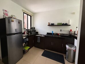 A compact kitchen with a refrigerator, microwave, and stove, a small window, and a trash bin. - Cumbres Novonorte: Private Pool, Covered Terrace & 3 Bedrooms (Mérida)