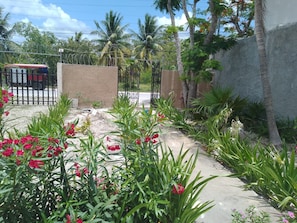 A gated entrance with a concrete pathway, surrounded by lush greenery and flowering plants.