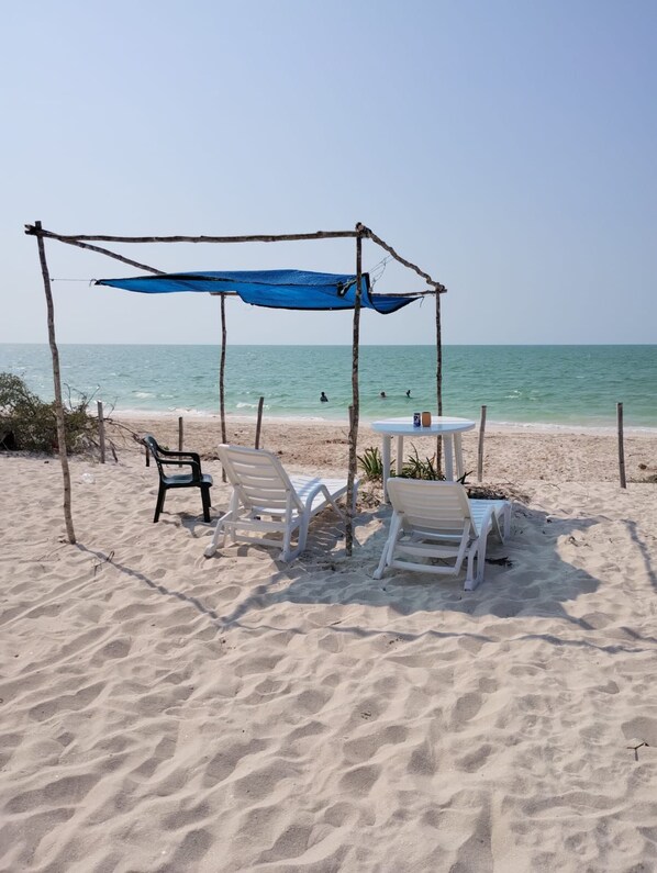 Une plage dotée d’un espace de repos ombragé, comprenant une table et des chaises, sous un auvent bleu.