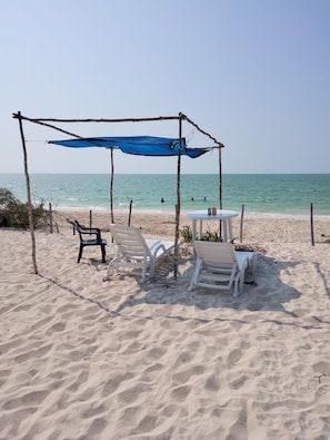 A beach with a shaded seating area, including a table and chairs, under a blue canopy.