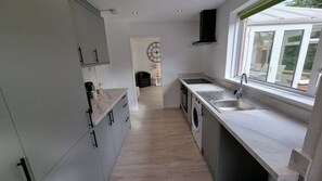 A compact kitchen with a washing machine, a sink, and a window providing a view of the outside. - Ayr 4 Bed House with Hot Tub available (South Ayrshire Council)