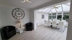 Ein modernes Interieur mit Essbereich, einem schwarzen Ledersessel, einem weißen Tisch und einer an der Wand befestigten Uhr.