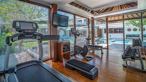 A modern gym with cardio equipment, weights, and a TV. - Villa Cendrawasih - 5BR Pool Villa & Gym, Walk to Batu Belig Beach Clubs (Badung)