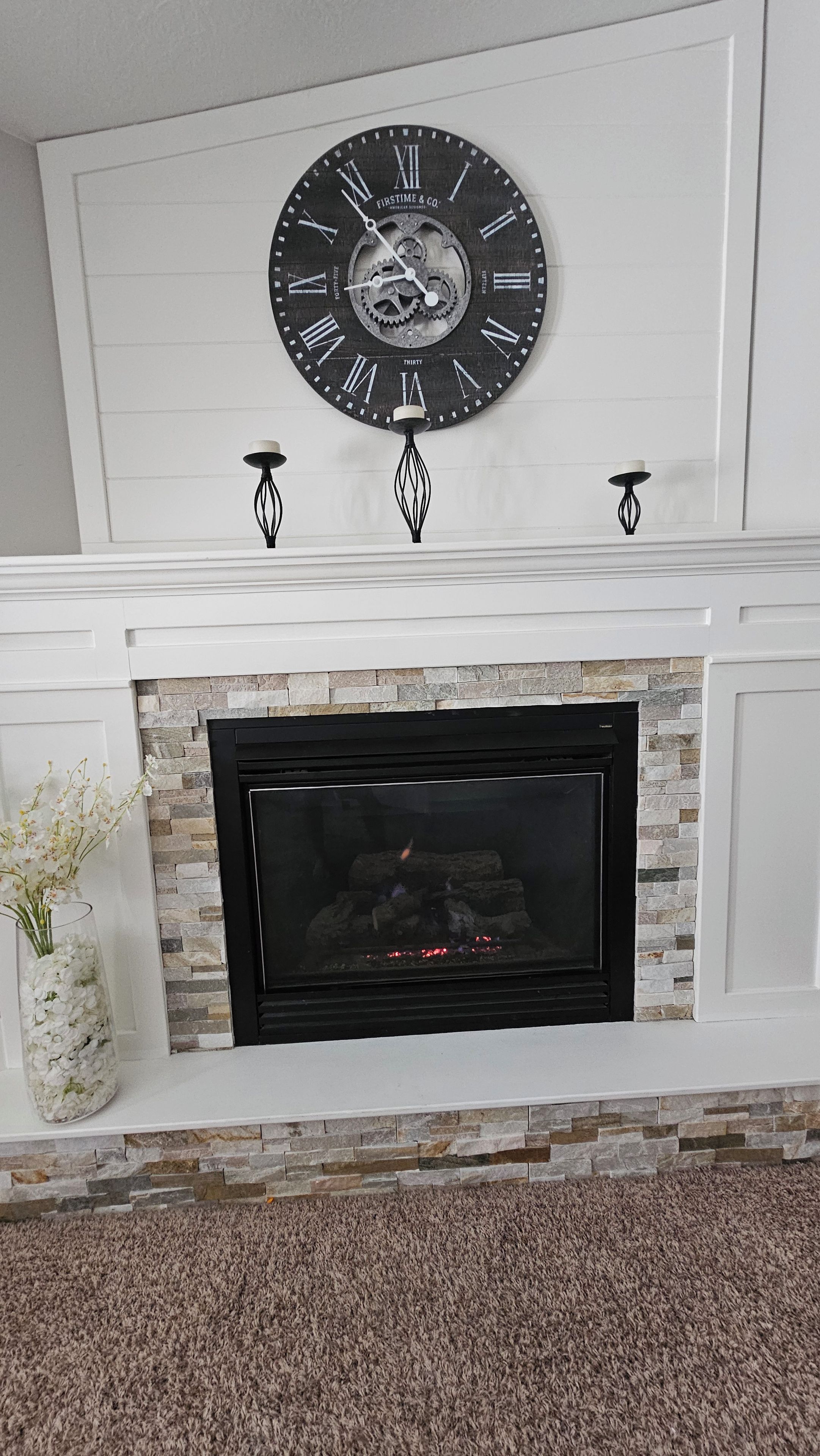 A fireplace with a stone surround, a black clock above it, and two wall-mounted candle holders.