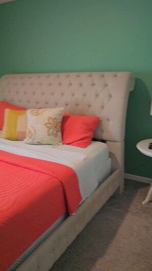 A bed with a tufted headboard, a red blanket, and multiple pillows.