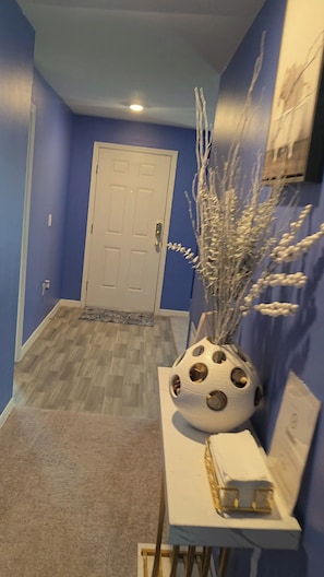 A hallway with a blue wall, a white door, and a decorative vase with branches. - Chic & Peaceful Retreat Close to It All (Port St. Lucie)