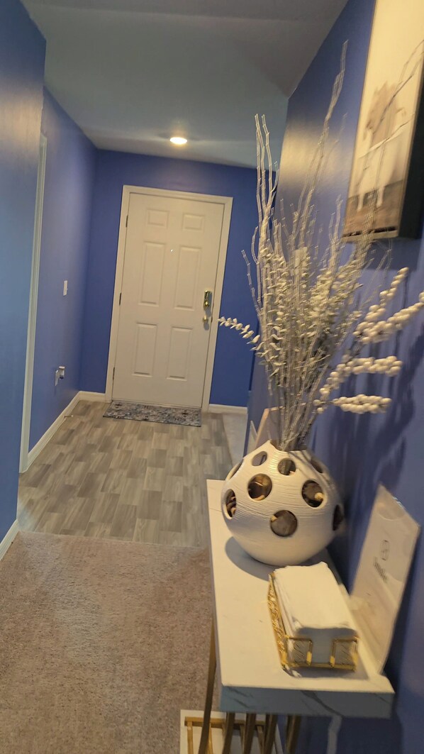 A hallway with a blue wall, a white door, and a decorative vase with branches.