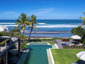 A pool area with a view of the ocean, palm trees, and outdoor seating. - NoKu Beach House - Beachfront 6BR Seminyak Villa, Sunsets & Full Staff (Badung)