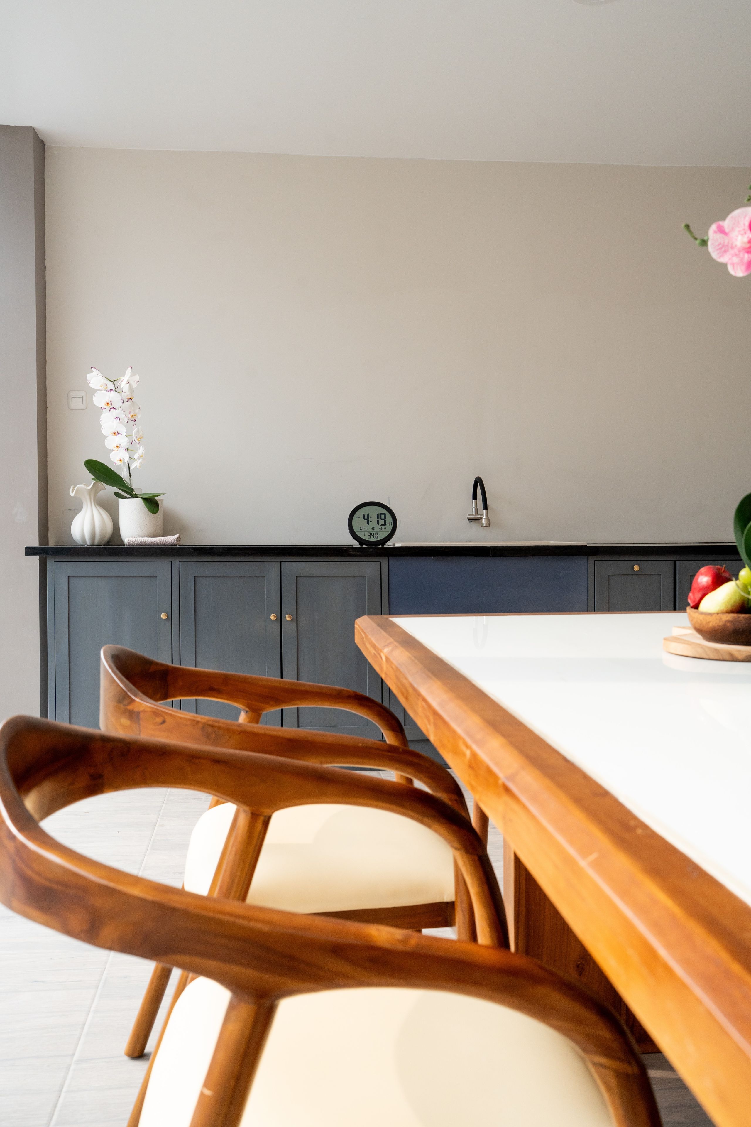 Una cocina moderna con una mesa de madera, sillas, un reloj y un florero con flores.
