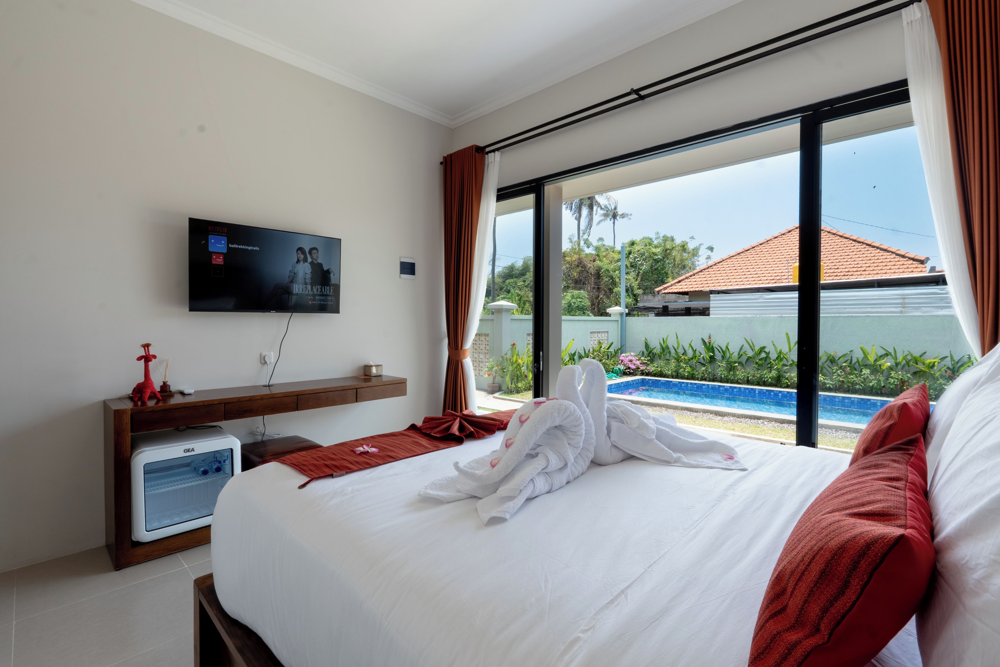 Een hotelkamer met een bed, een televisie, een bureau en uitzicht op een zwembad.