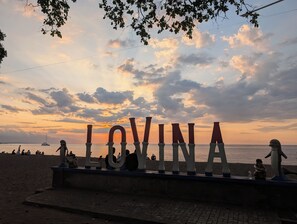 A beach with a large sign spelling 'LOVINA' and people sitting on the sand. - Emiloka Villa (Buleleng)