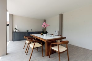 Un comedor moderno con una mesa y sillas de madera, una cocina al fondo y vistas al exterior.
