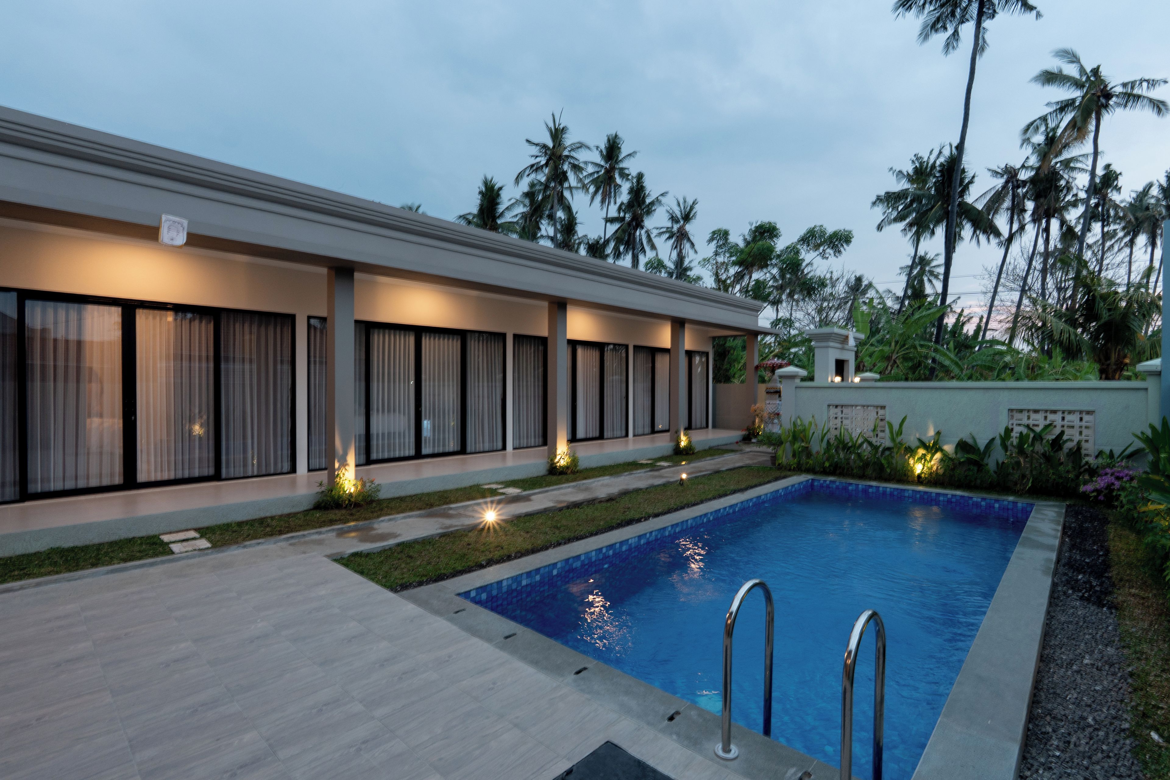 A modern hotel with a swimming pool, large windows, and palm trees in the background.
