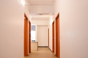 Un pasillo con puertas de madera y piso de baldosas, que conduce a una habitación con ventana.