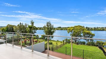 A balcony with a view of a lake, surrounded by greenery and a clear sky.