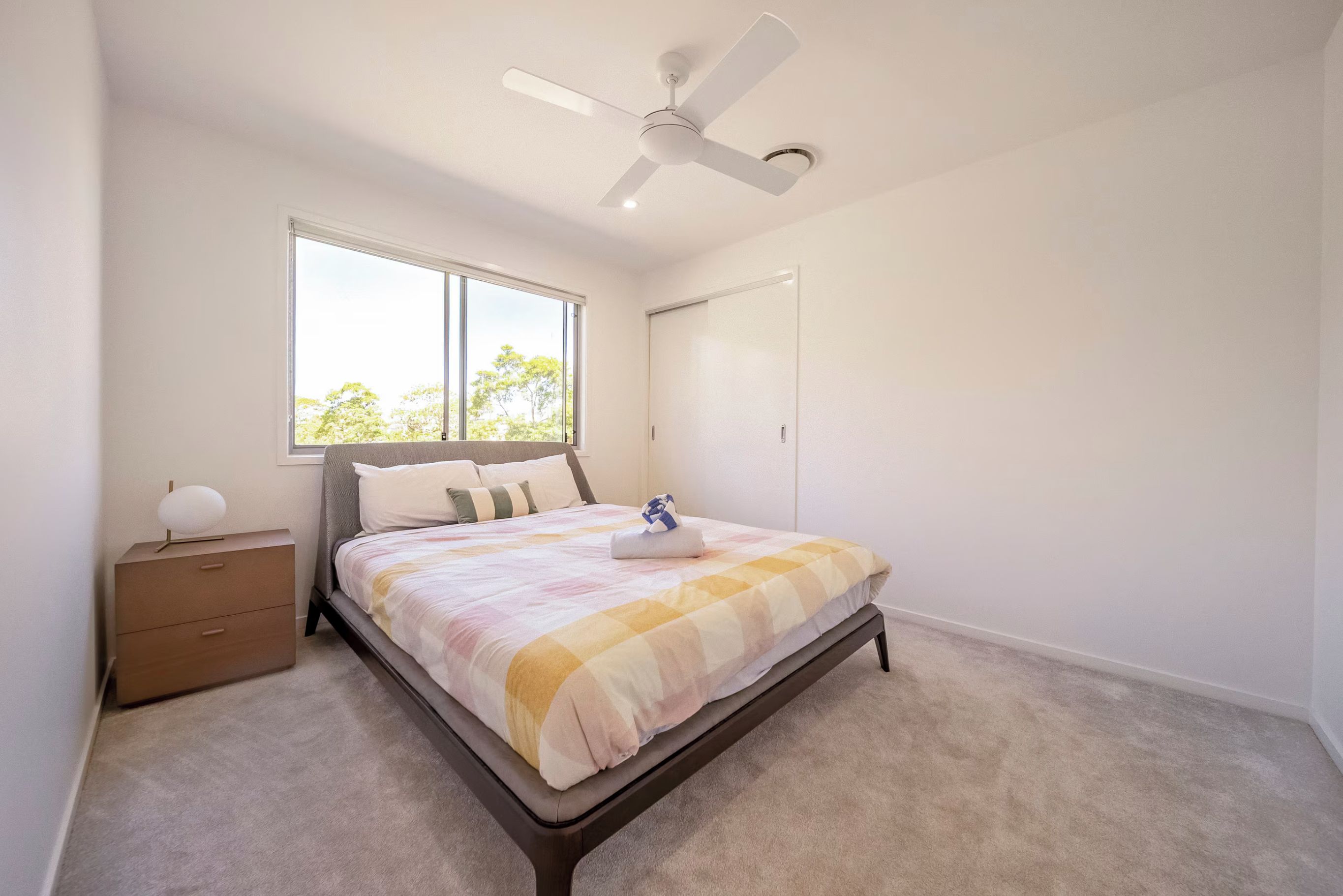 A bedroom with a bed, a nightstand, a window, and a ceiling fan.