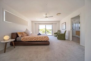 Ein modernes Schlafzimmer mit einem großen Bett, einem Deckenventilator und Blick ins Freie.